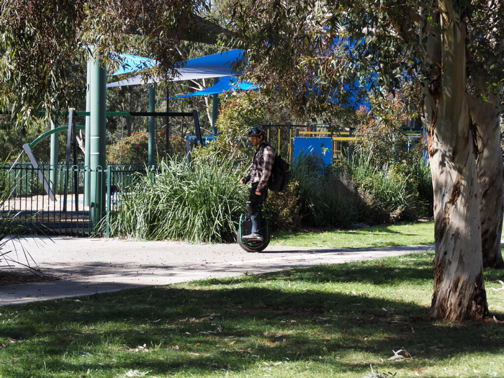 A man riding a modern unicycle through a park by a playground